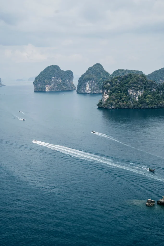 Speedboats and longtail boats crossing turquoise water between limestone islands in the Andaman Sea