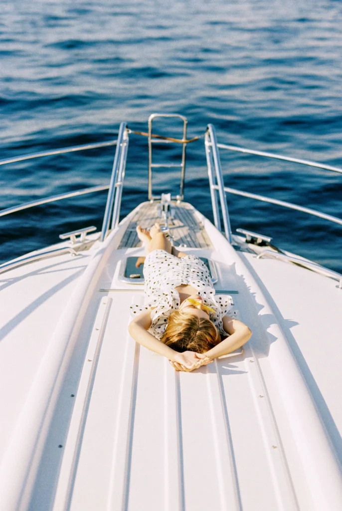 Guest sunbathing on the bow of a yacht over deep blue water